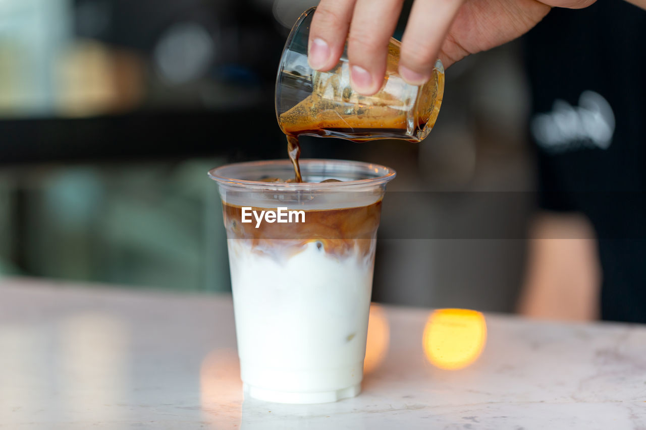 Barista preparing ice latte, pouring coffee into plastic cup with milk