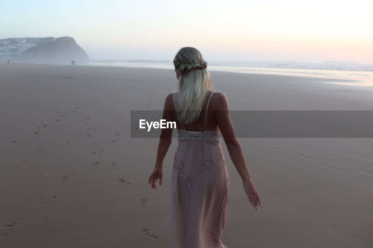 REAR VIEW OF A WOMAN STANDING ON BEACH