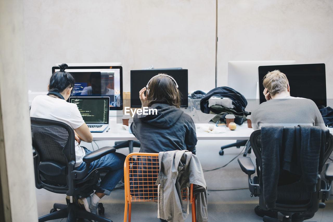 Rear view of programmers using computers at desk in office