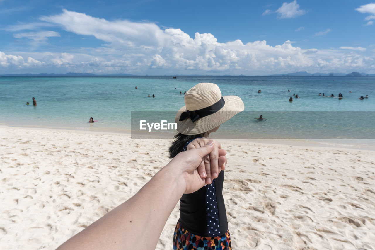 Woman holding hand at beach against sky