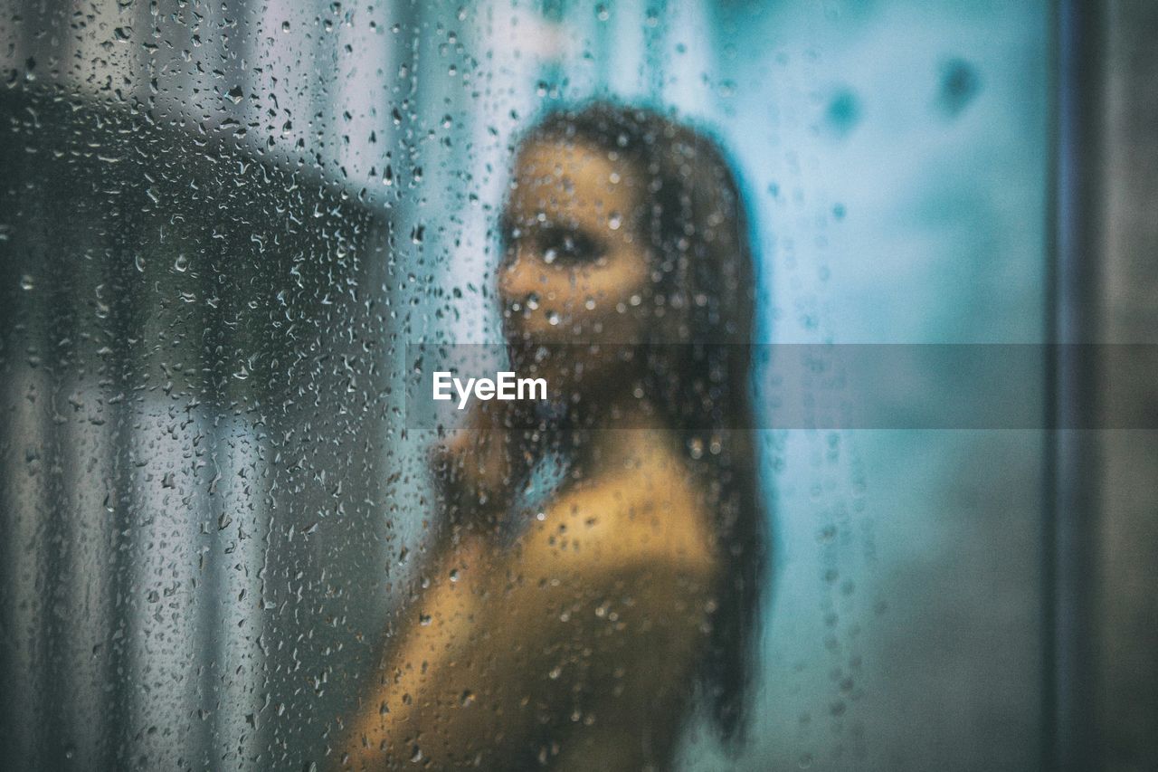 Side view of young woman bathing in bathroom seen through glass