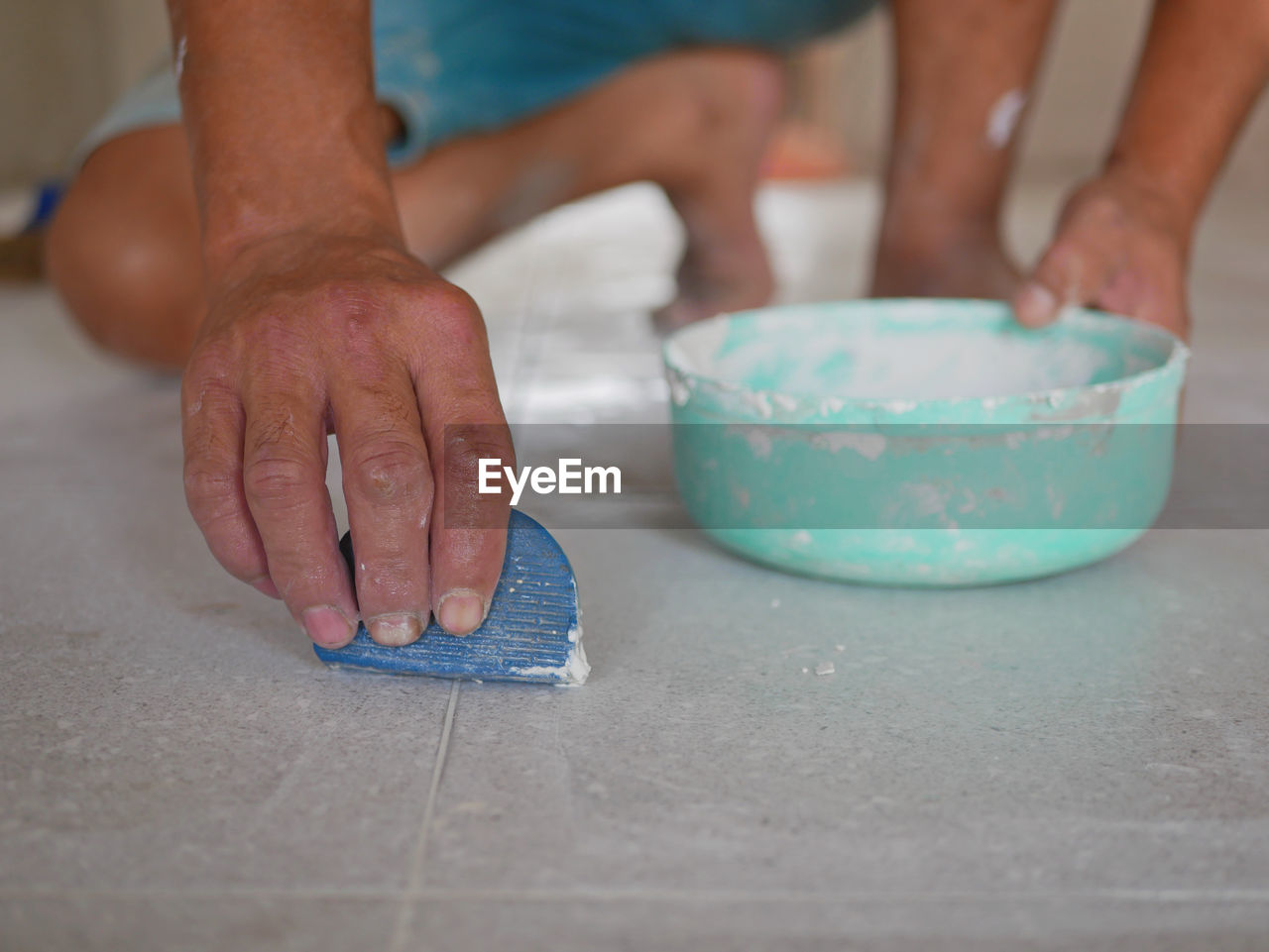 Low section of man applying cement on tiled floor