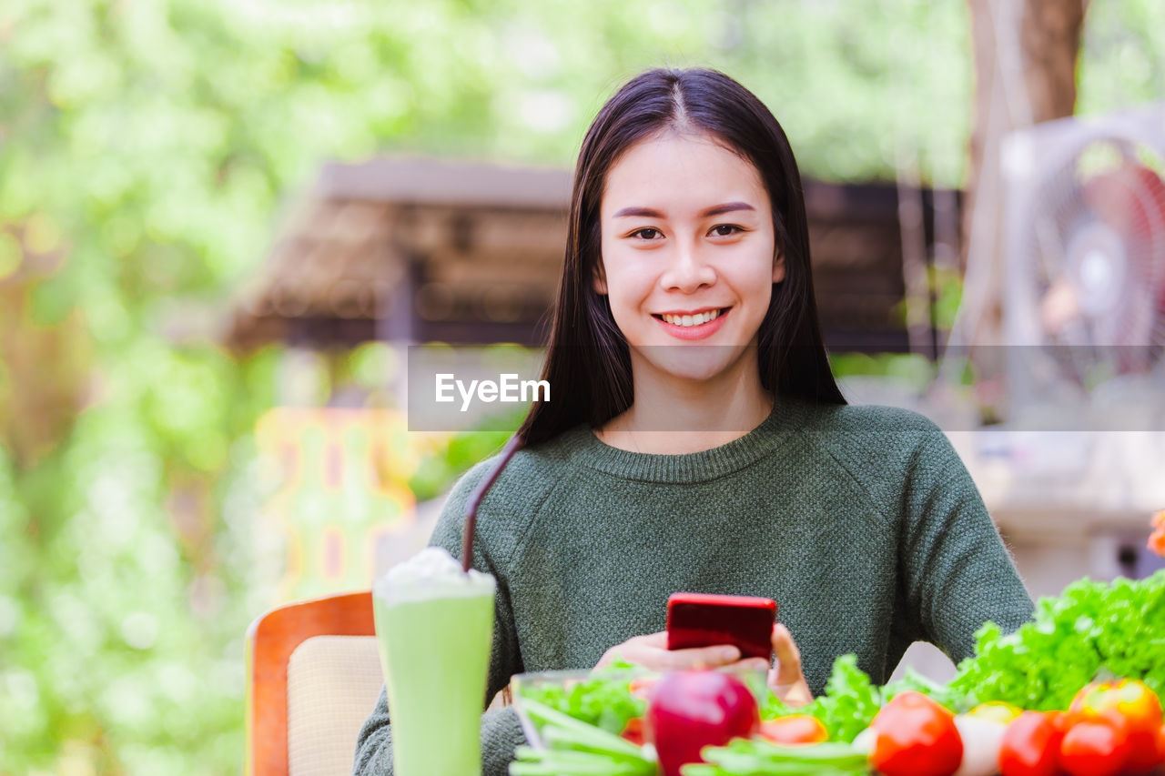 Portrait of smiling woman holding mobile phone by vegetables