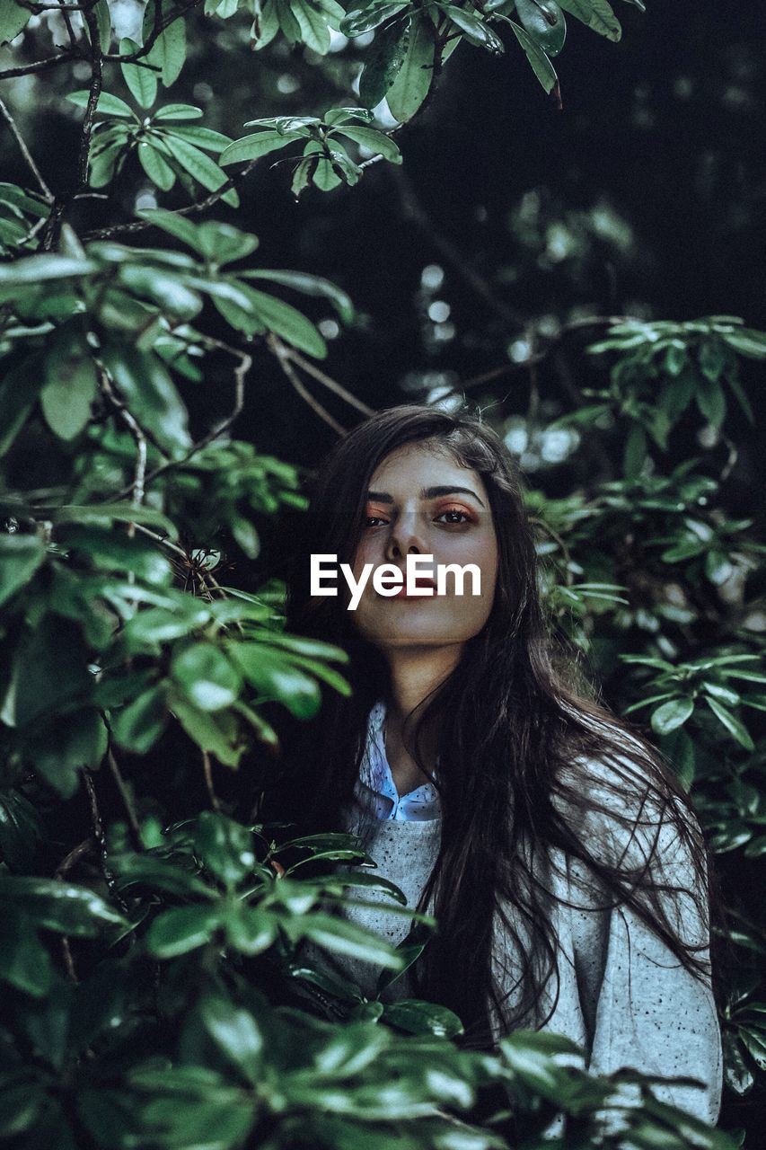 Portrait of young woman standing by plants