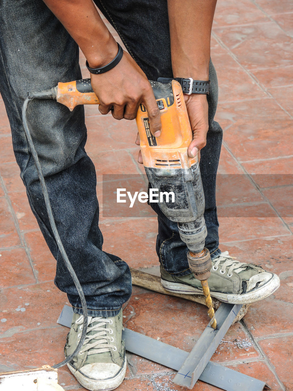 Low section of worker drilling metal on walkway 