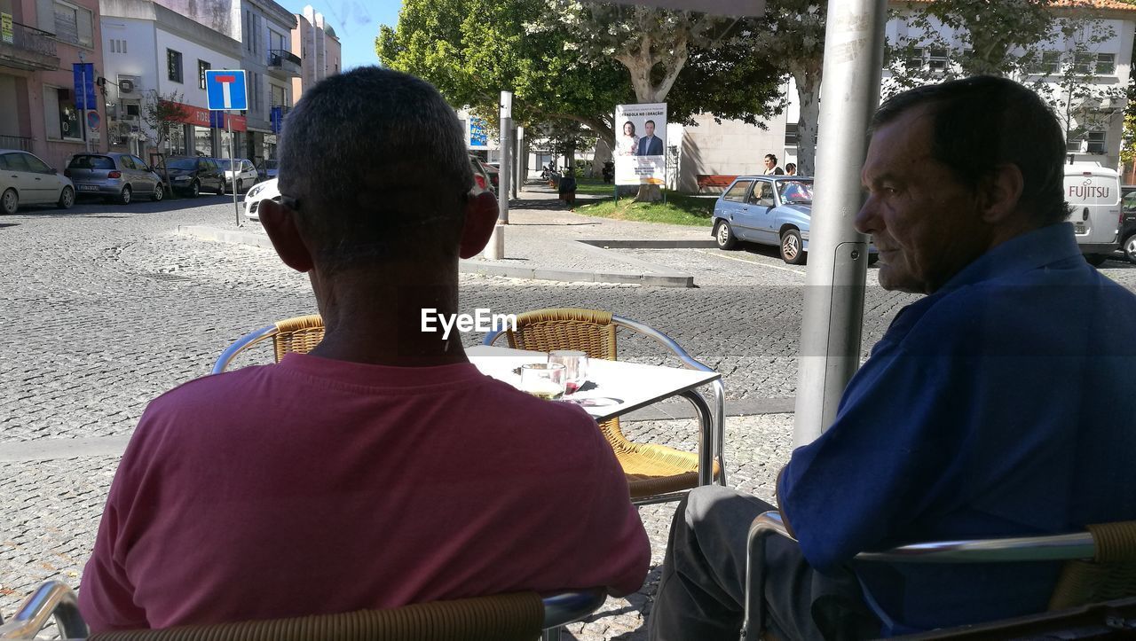 REAR VIEW OF MAN SITTING AT SIDEWALK CAFE