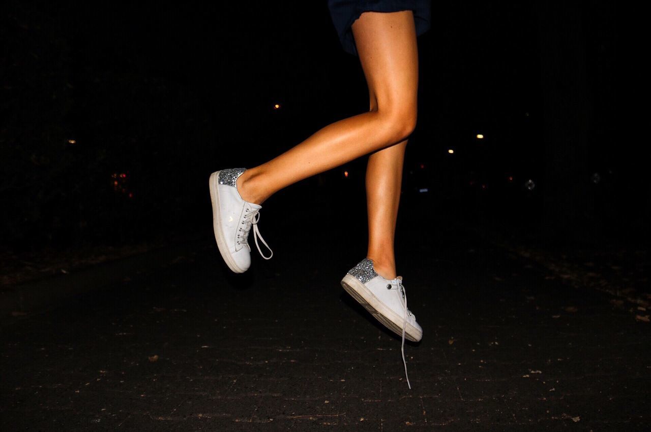 Low section of girl jumping on footpath at night