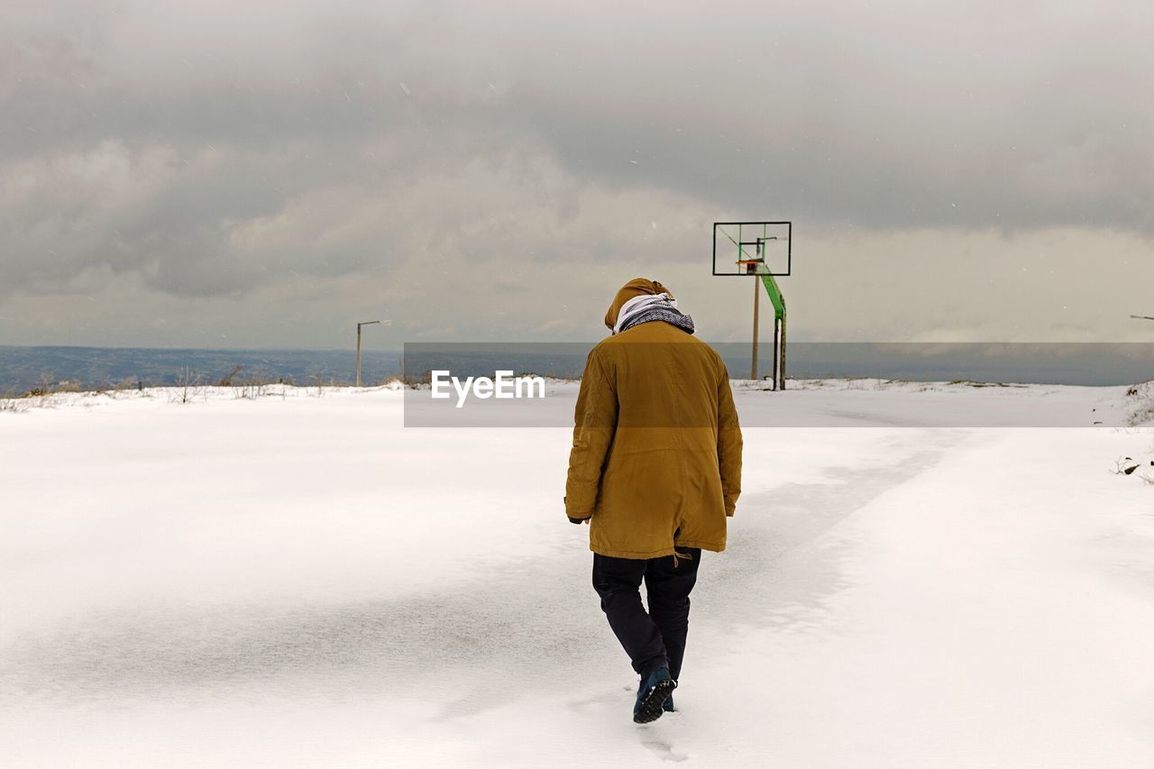 Rear view of man walking on snow covered landscape