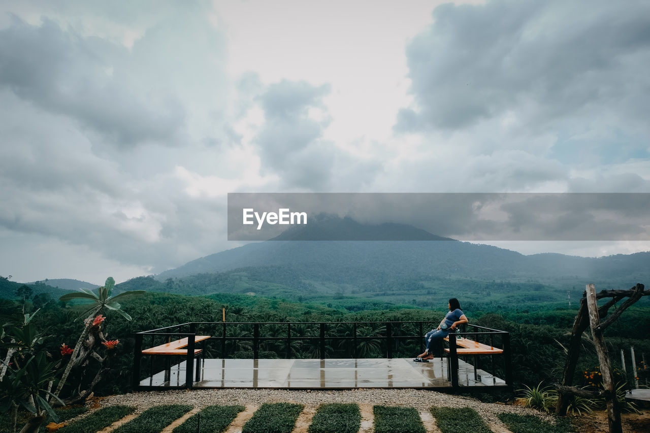 PEOPLE SITTING ON BENCH AGAINST MOUNTAIN RANGE