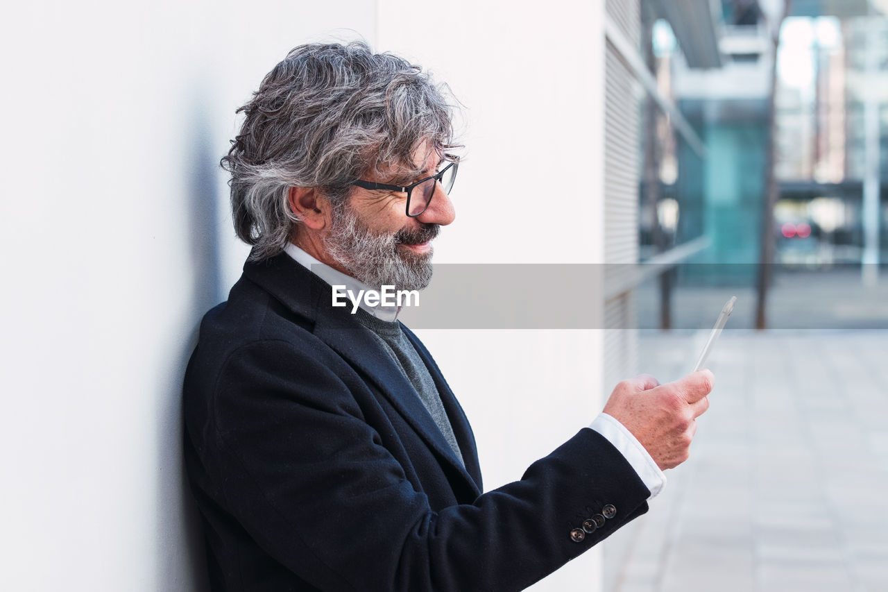 Senior businessman using mobile phone, typing message to partners after conference