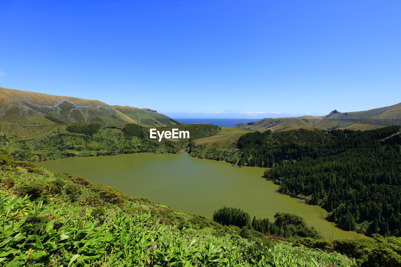 Scenic view of lake and mountains against clear blue sky