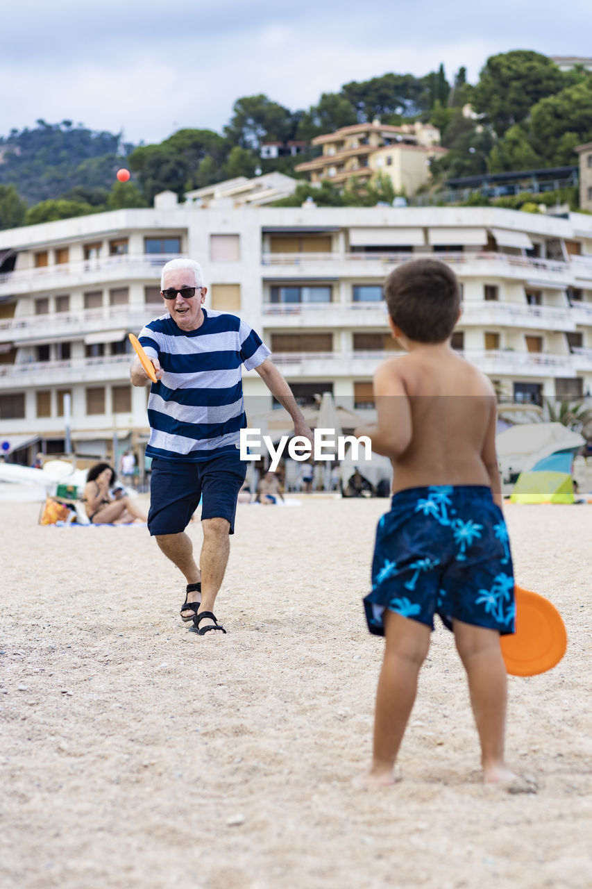 Rear view of boy playing with grandfather on beach