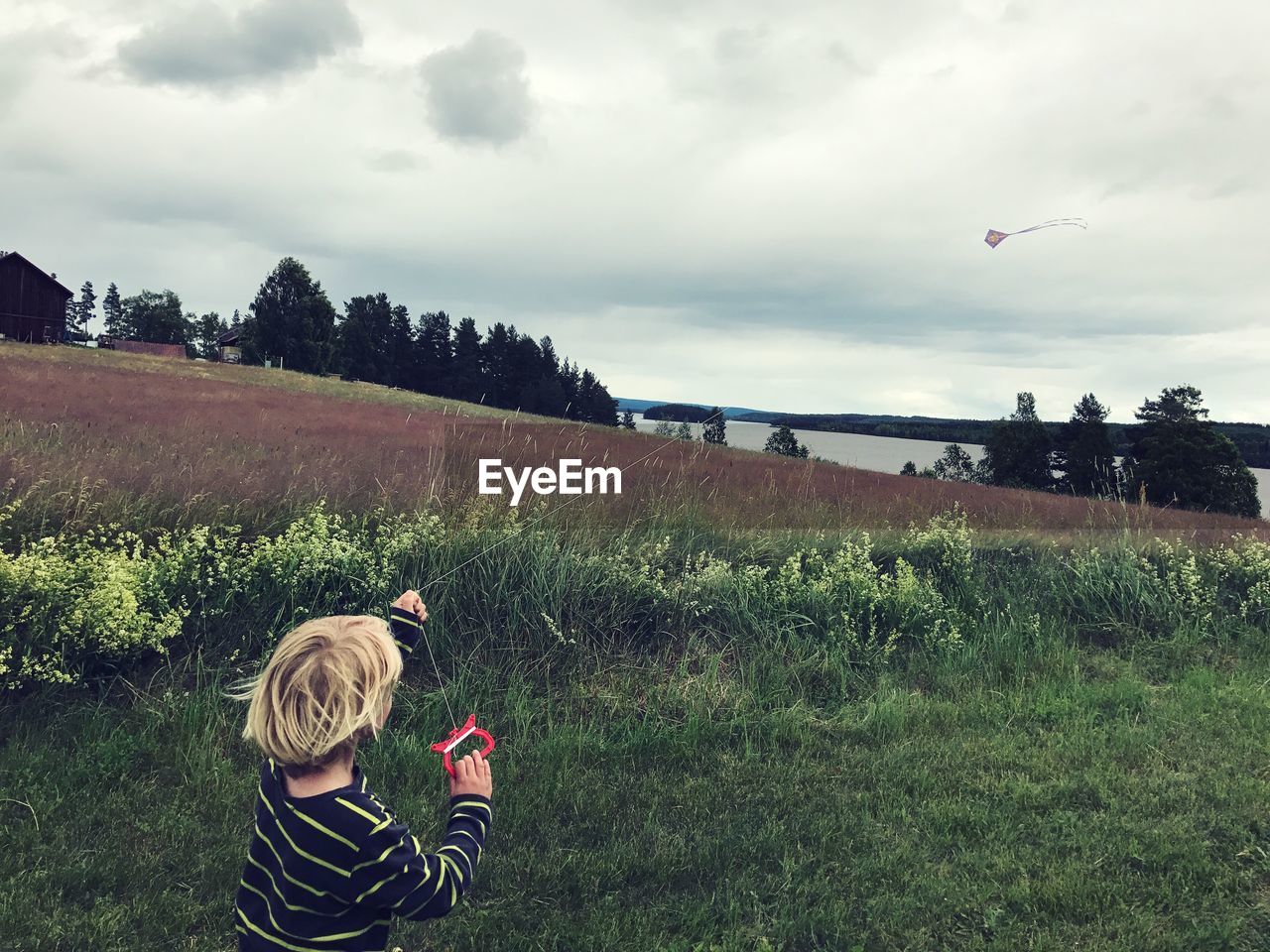 Child flying kite on field against sky