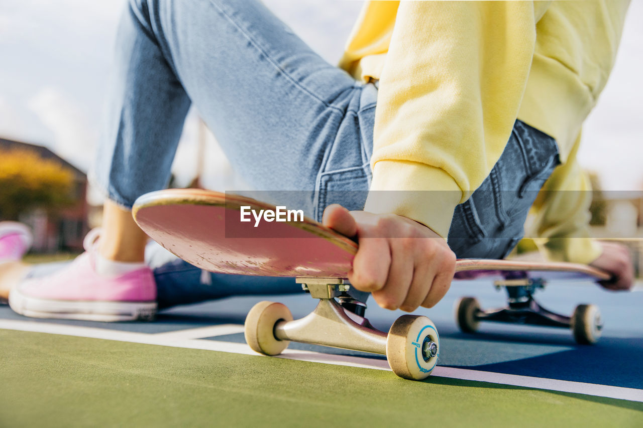 Close up of skateboard with girl sitting on it on a tennis court