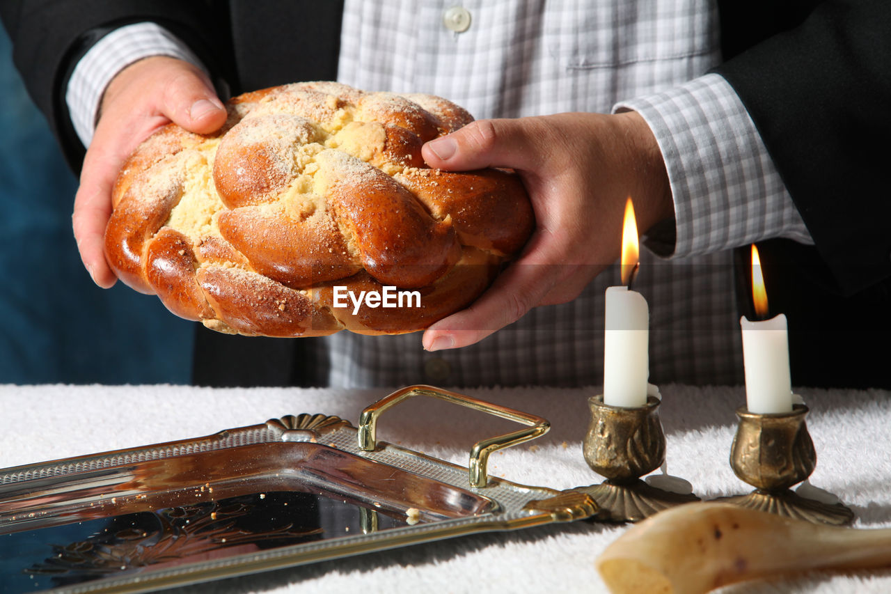 Midsection of man holding bread with lit candles on table