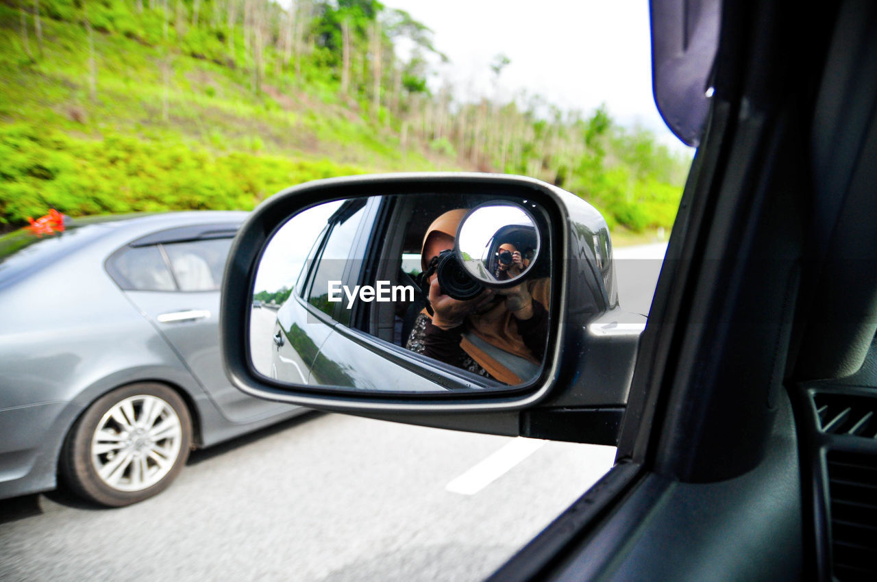 Reflection of woman photographing in side-view mirror