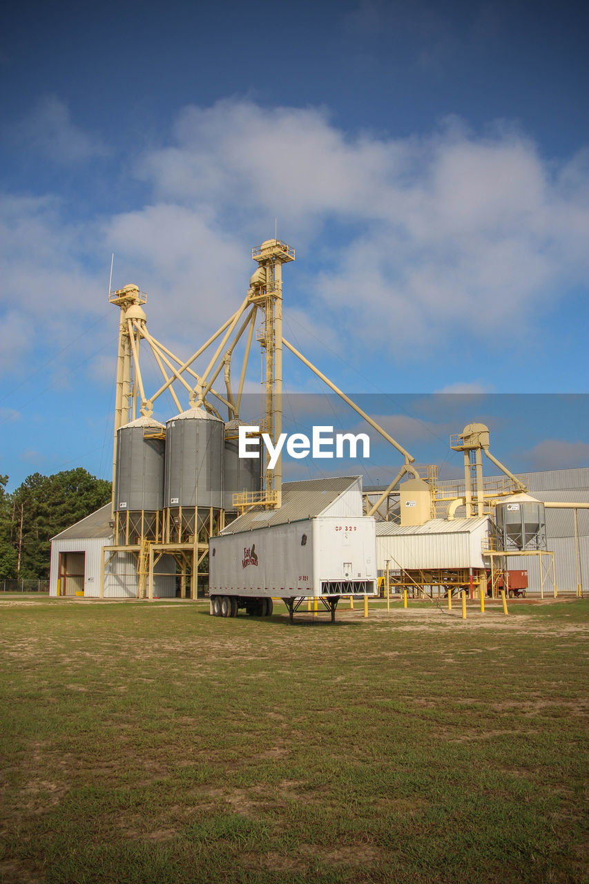 Vehicle trailer on field at factory against blue sky