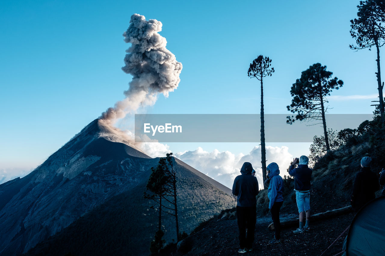 Rear view of hikers looking at acatenango volcano against blue sky