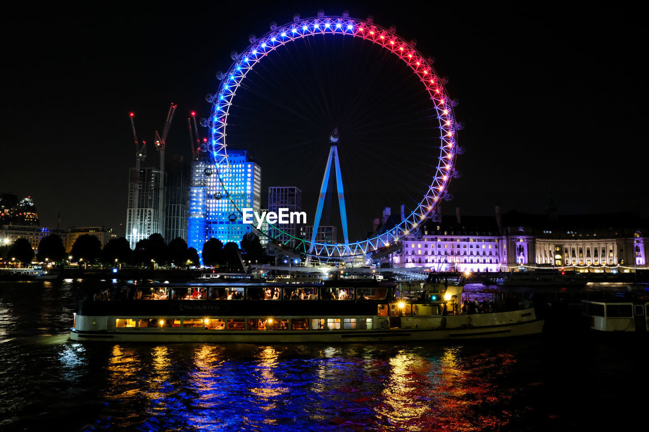 ILLUMINATED FERRIS WHEEL BY RIVER AT NIGHT