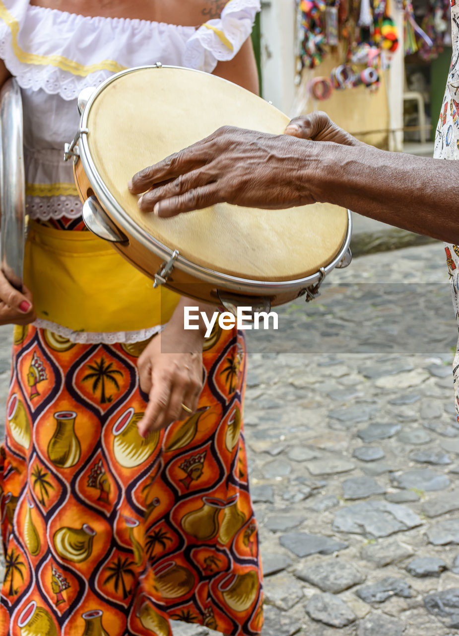 Tambourine player with a woman in typical clothes in the background in pelourinho, salvador, bahia