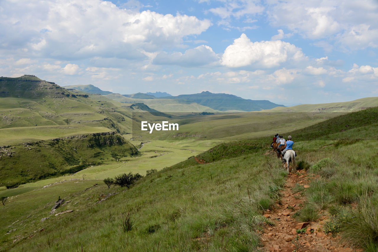 Rear view of people riding horses on mountain against cloudy sky