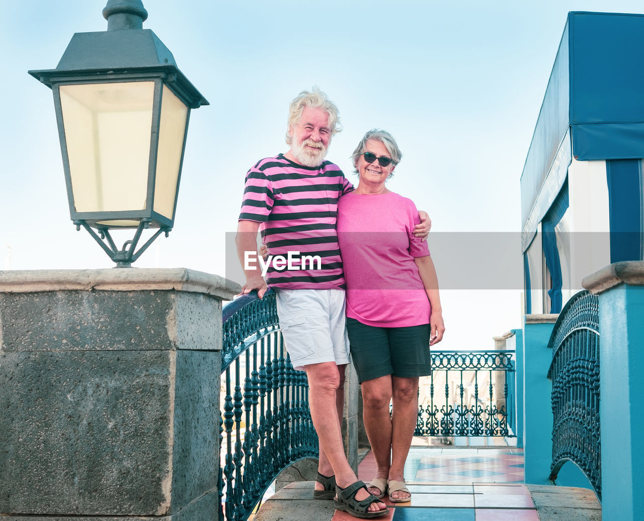Portrait of senior couple standing by railing against sky