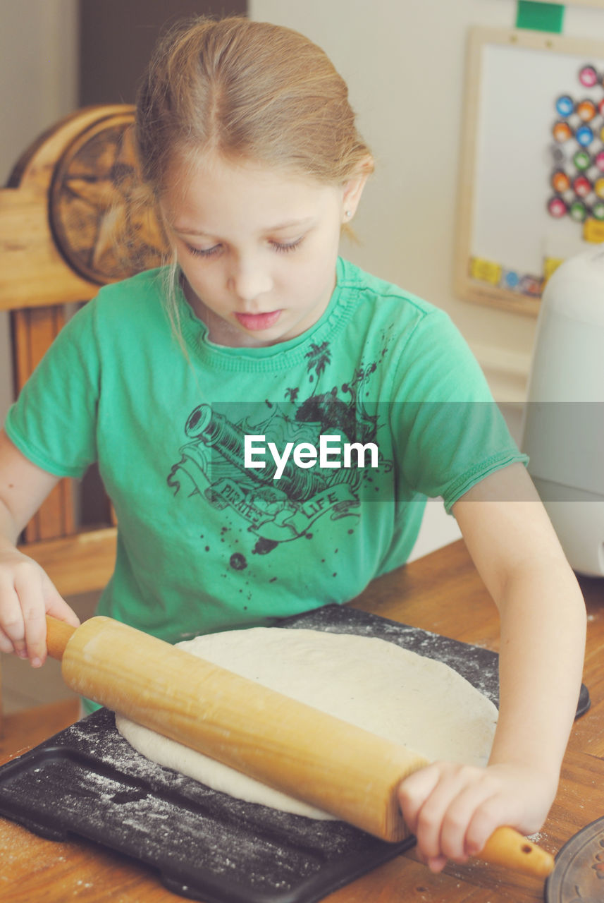 Girl rolling dough for pizza at table