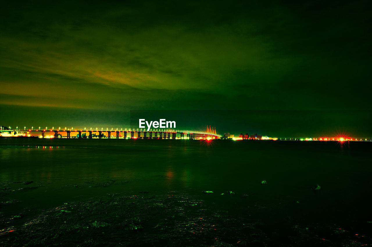 ILLUMINATED BRIDGE OVER RIVER AT NIGHT