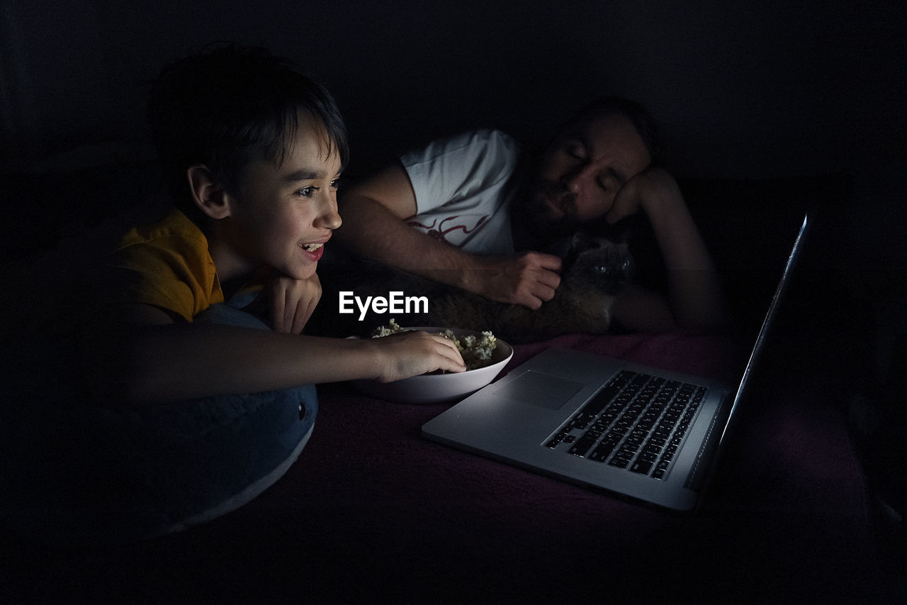 Boy with food looking at laptop by father