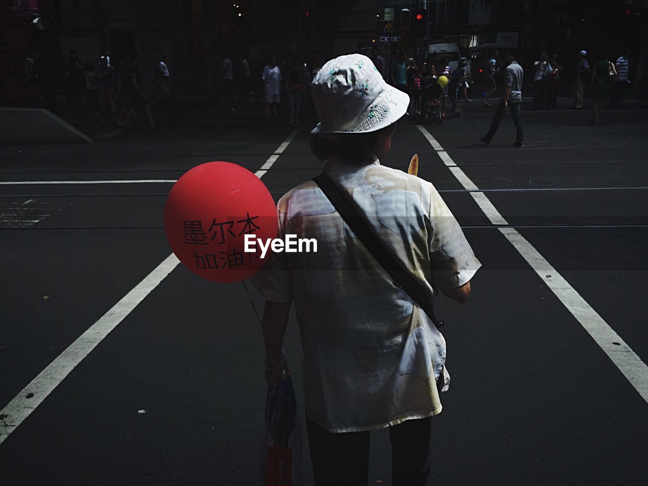 Rear view of person holding red balloon on street