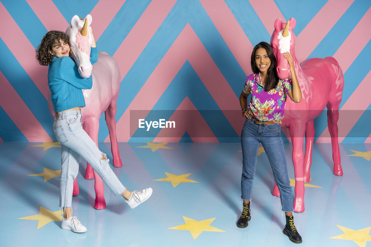 Two happy young women at an indoor theme park with unicorn figures