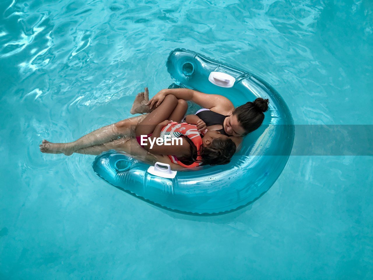High angle view of woman with girl relaxing on inflatable chair in swimming pool