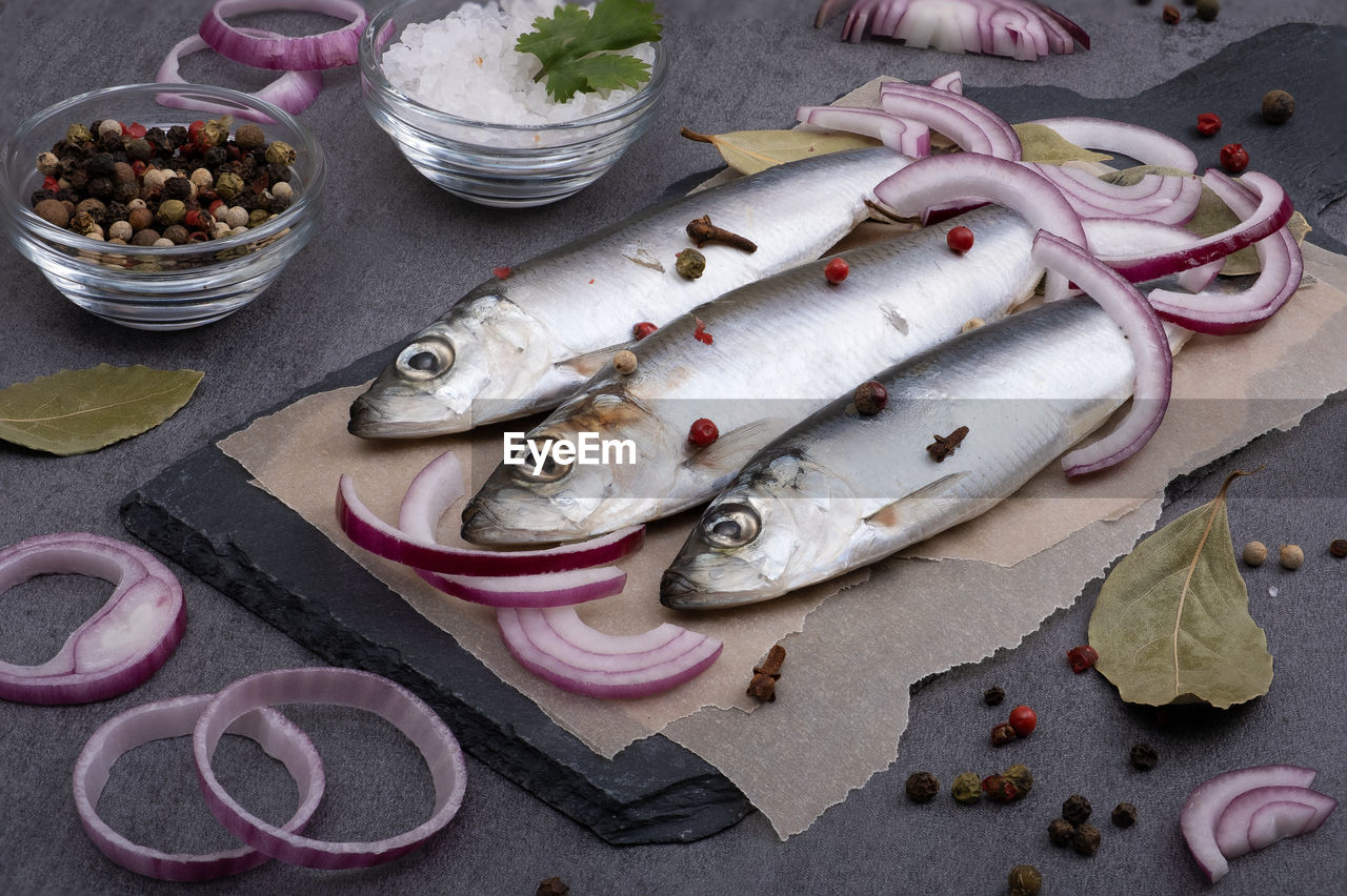 Close-up top view of several pickled herrings with spices on parchment paper on a serving board. 