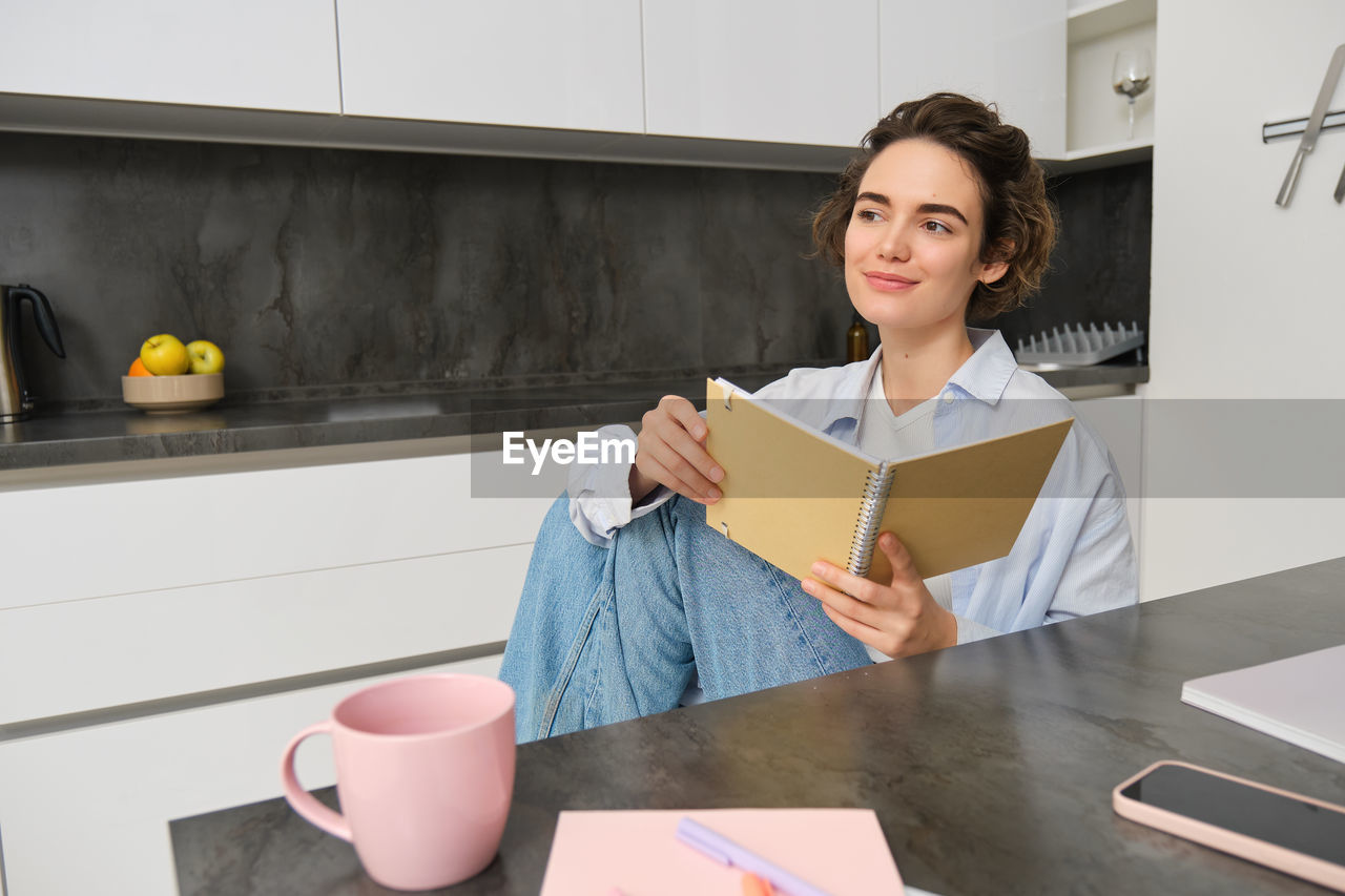 portrait of young woman using digital tablet while sitting on table at home