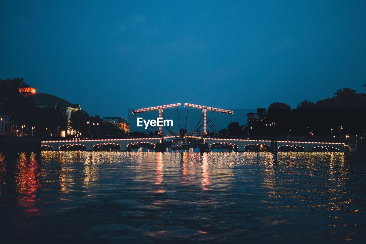 Illuminated bridge over river against sky at night