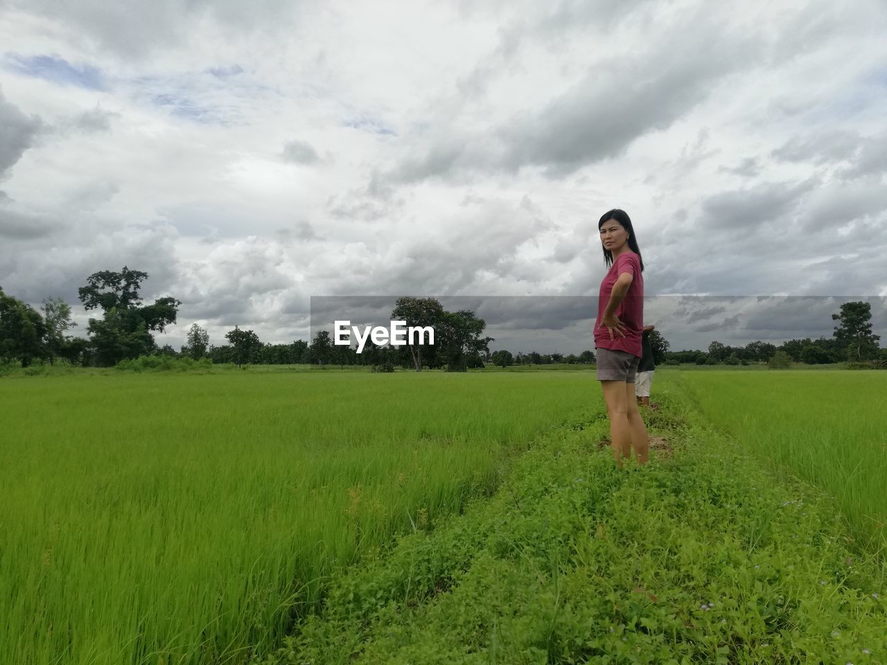 Portrait of woman standing on field against cloudy sky