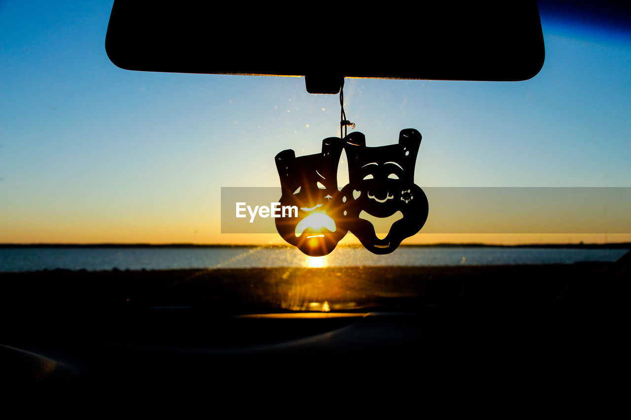 Silhouette decoration on rear-view mirror of car against clear sky