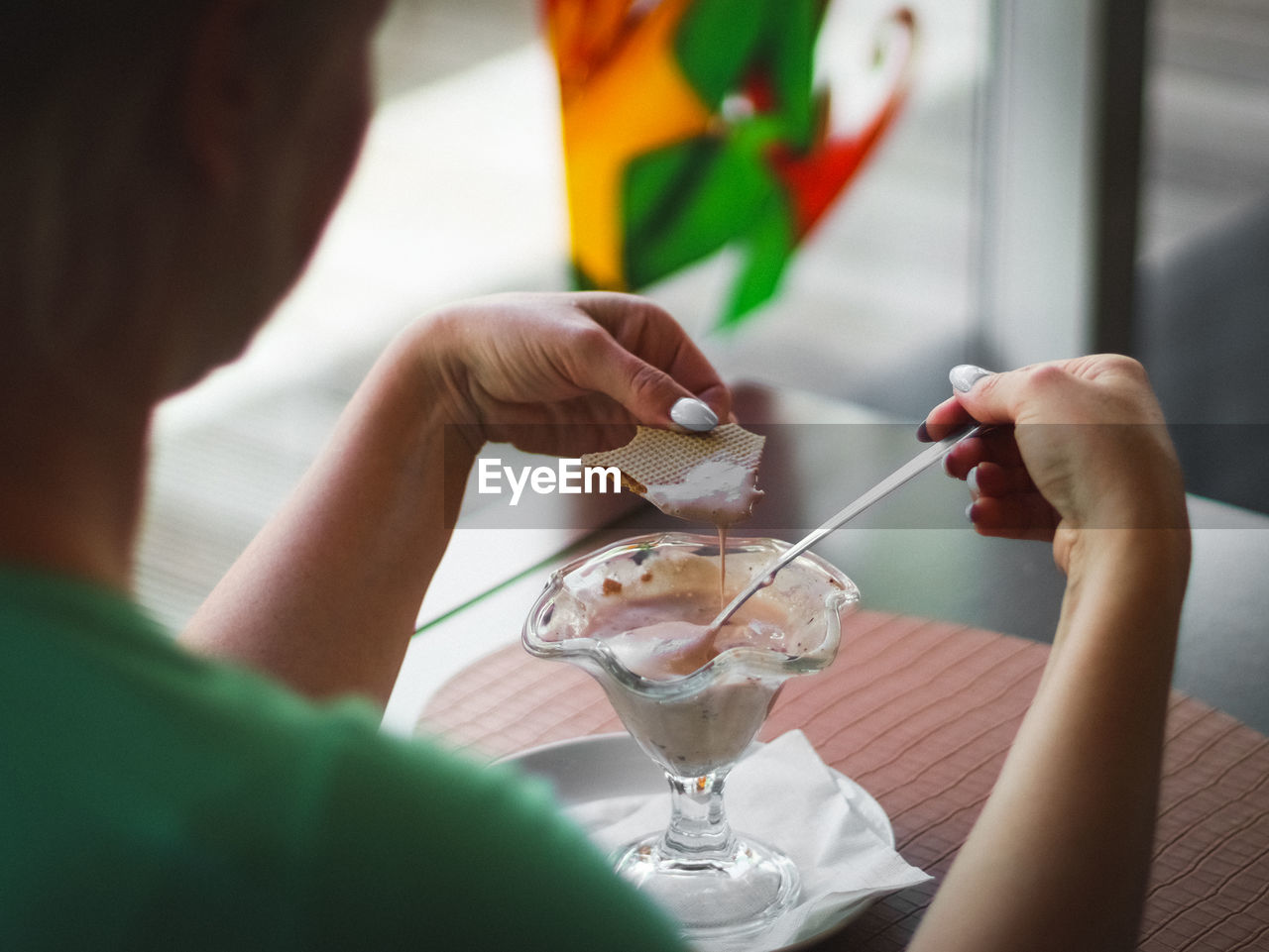 A young caucasian woman sits alone at a table inside a cafe and eats melted strawberry ice cream