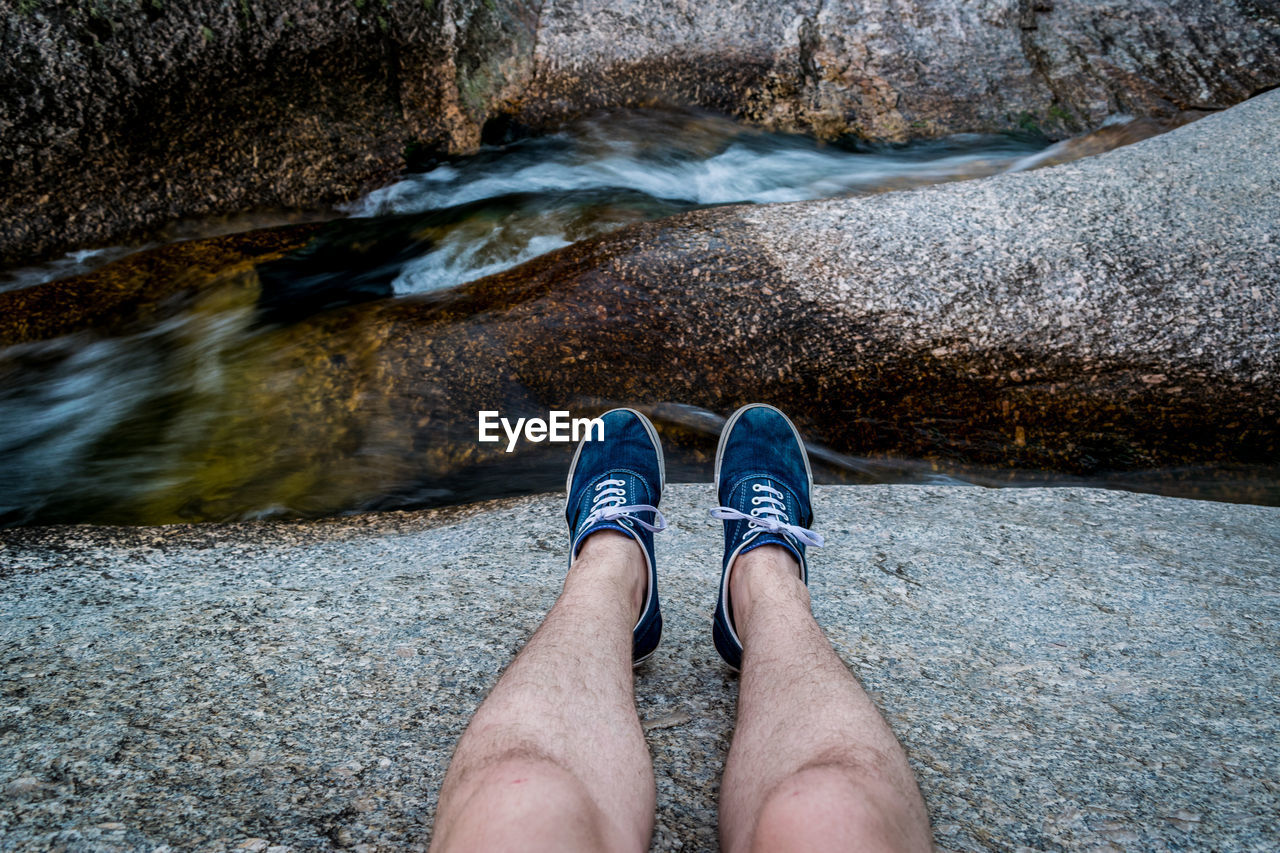 Low section of man on rock by stream