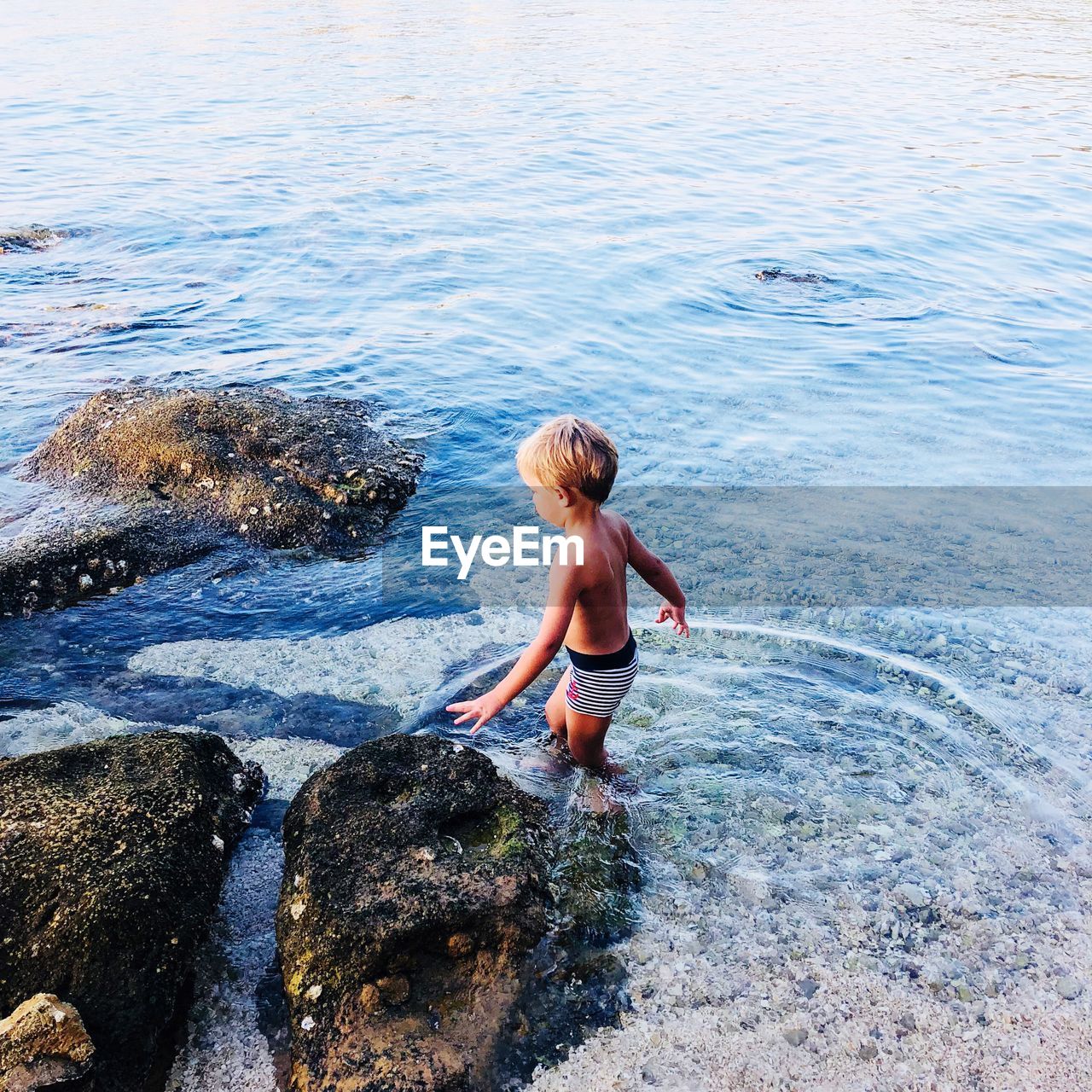 HIGH ANGLE VIEW OF SHIRTLESS BOY ON ROCKS AT SEA