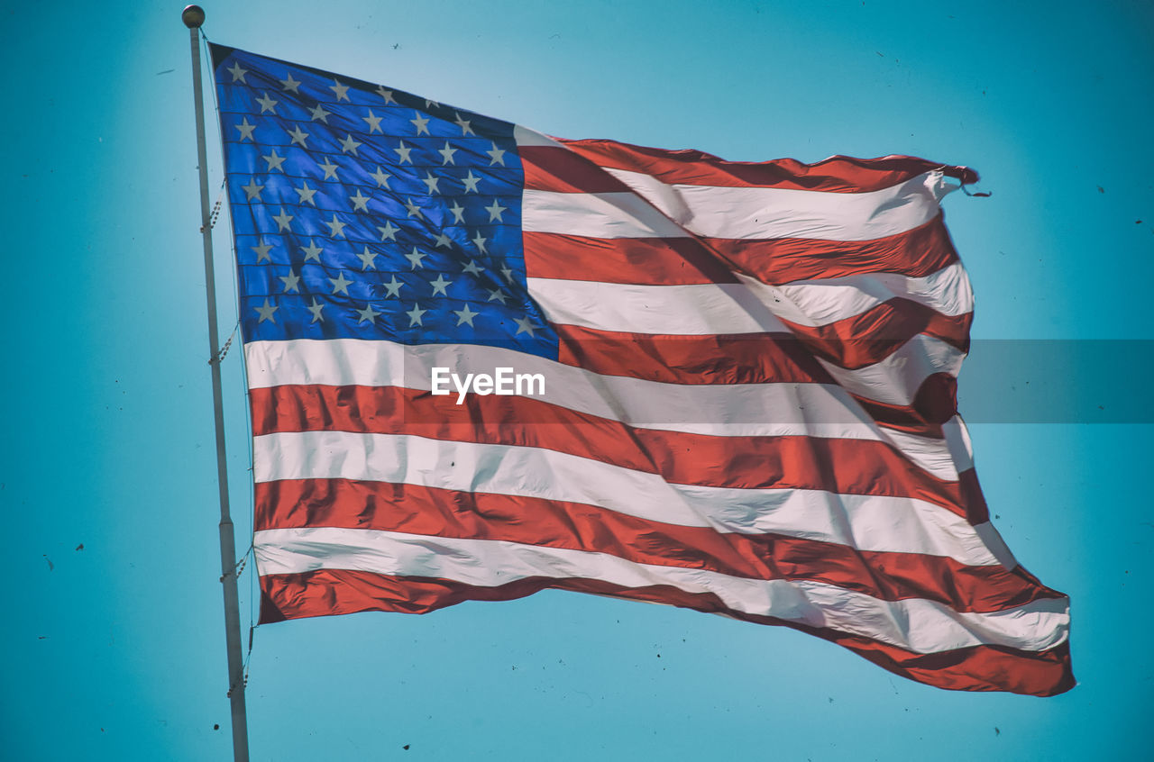 Low angle view of american flag waving against blue sky