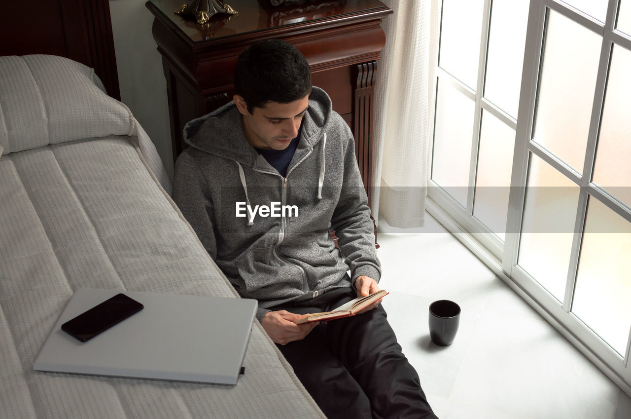 YOUNG MAN USING MOBILE PHONE WHILE SITTING ON LAPTOP