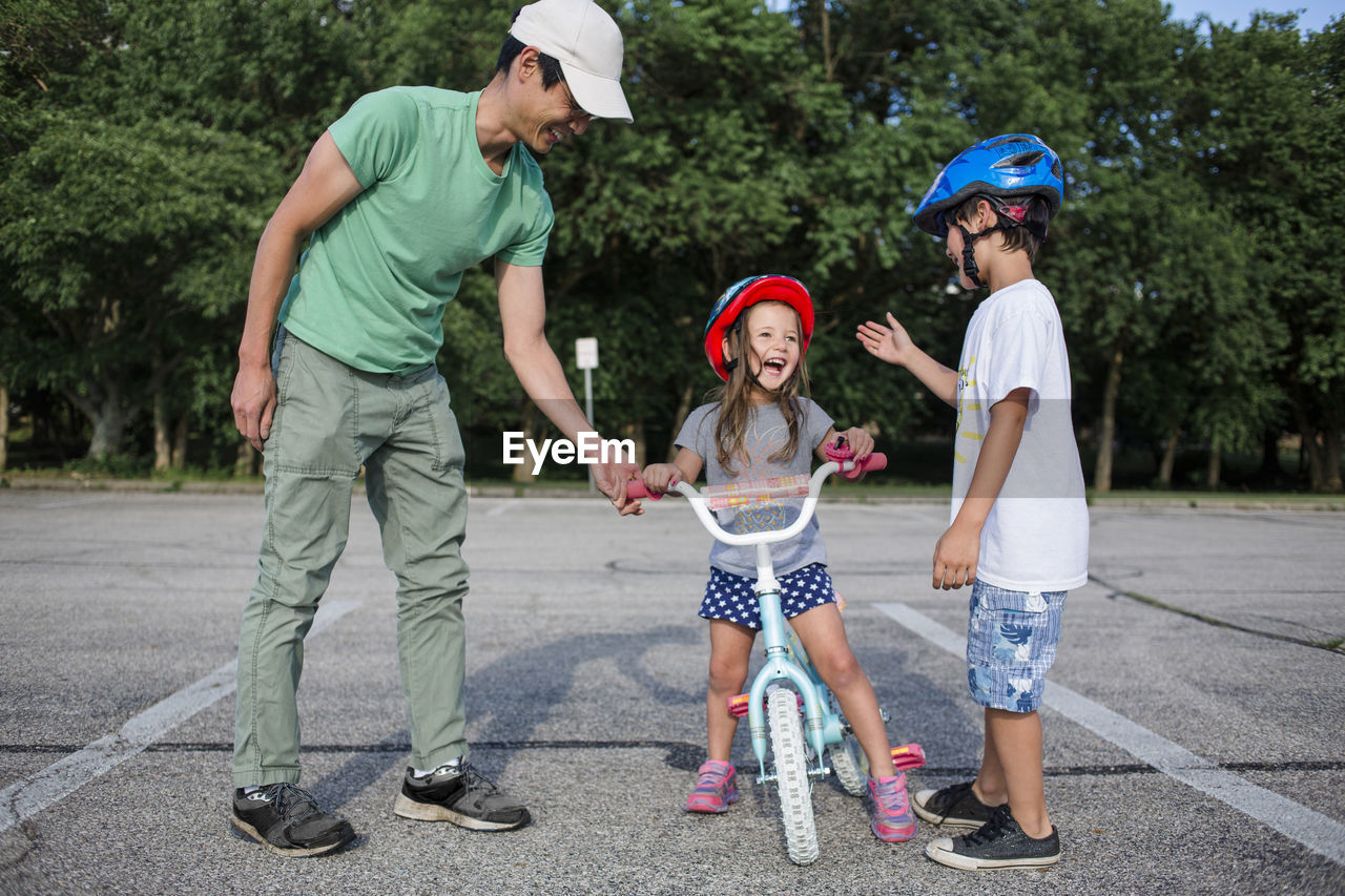 Cheerful girl learning cycling with father and brother at playground