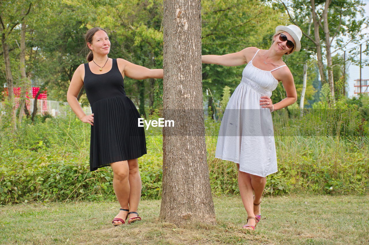 Portrait of women standing by tree trunk in park