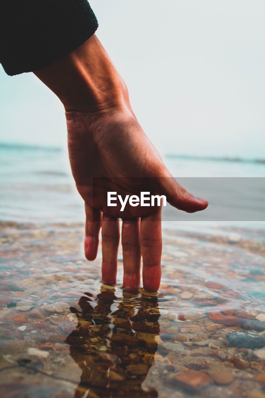 Close-up of man touching water in sea against sky