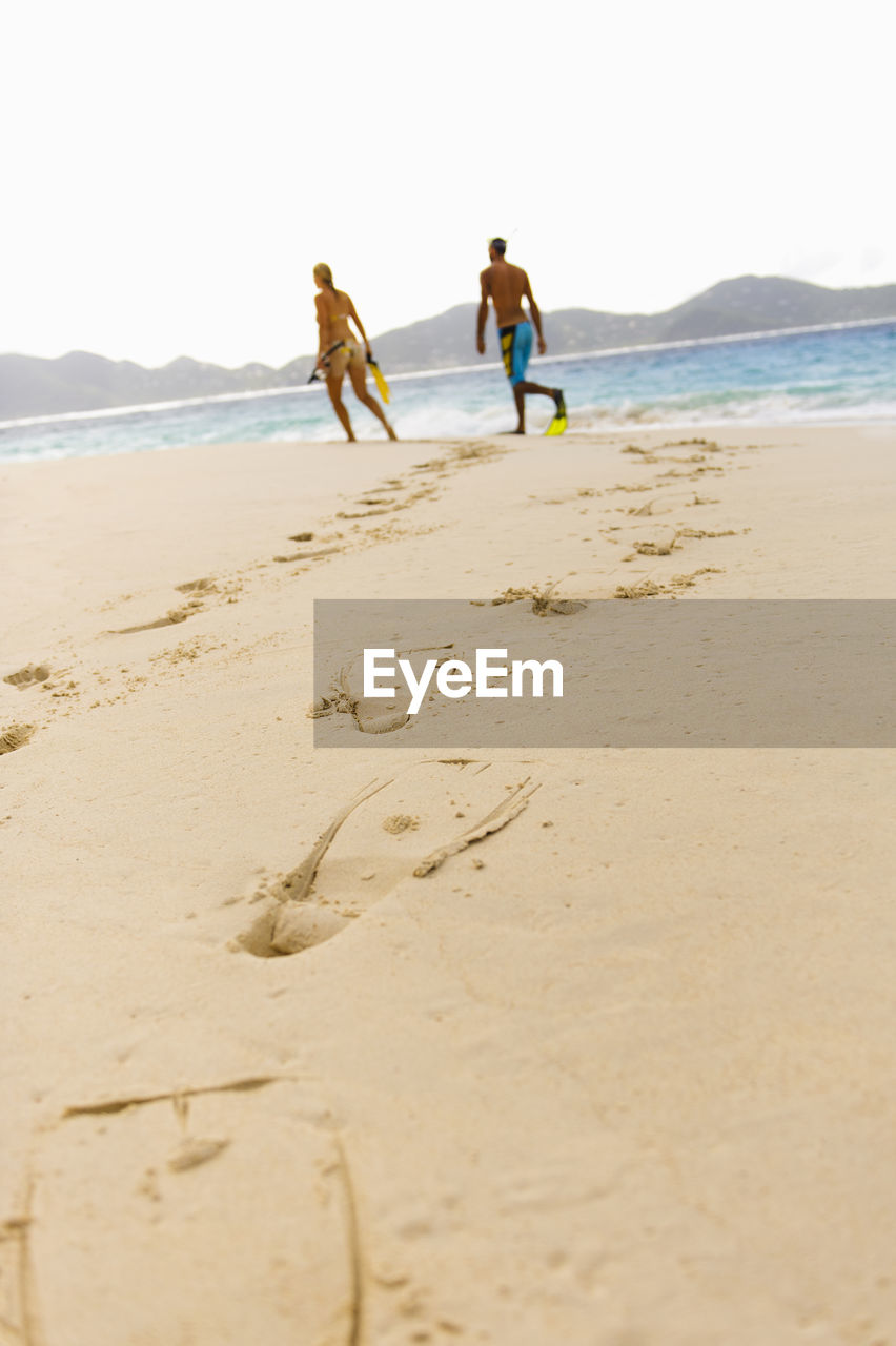 Diving flipper prints on sand, mid adult couple in background