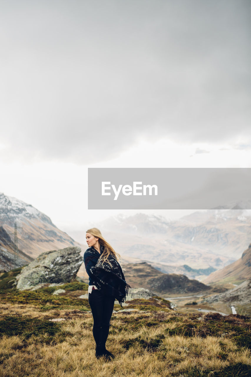 Young woman standing by mountain against sky