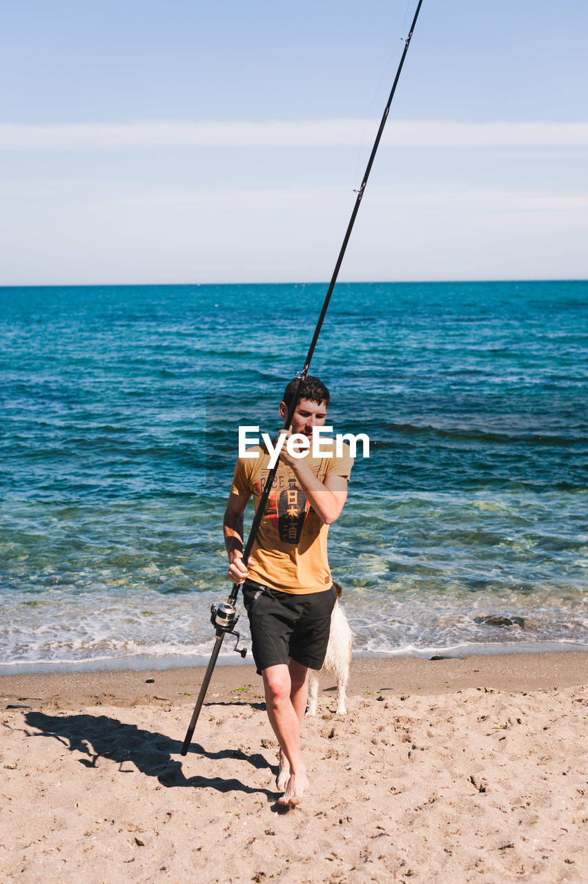 Man holding fishing rod while walking with dog at beach