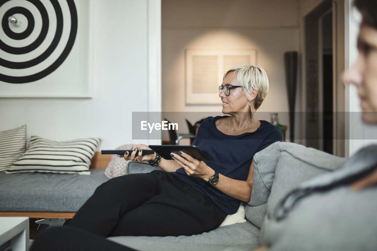 Industrial designer using remote control while sitting with colleague on sofa at home