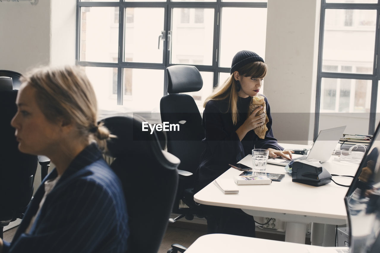 Businesswoman eating food while working on laptop at office